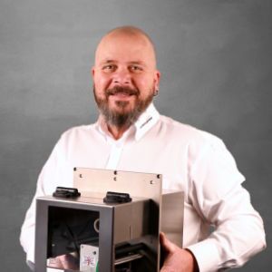 Michael Looser, Technischer Verkäufer bei WILUX PRINT, hält ein Hochleistungsmodul in den Händen, professionell gekleidet in einem weissen Hemd, vor einem neutralen Hintergrund.