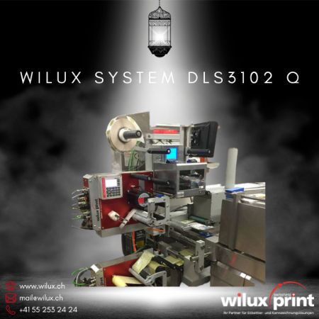 Automatischer Etikettenspender WILUX System DLS3102 Q mit rotem Gehäuse, ausgestattet mit Thermotransferdrucker und Steuerungseinheit, geeignet für die präzise Etikettierung von Verpackungen im Stillstand.