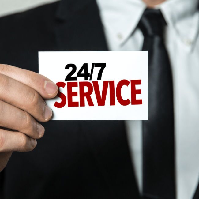 Mann im Anzug hält eine Karte mit der Aufschrift "24/7 Service" – symbolisiert den rund um die Uhr verfügbaren Pikettdienst von WILUX für schnelle Unterstützung.