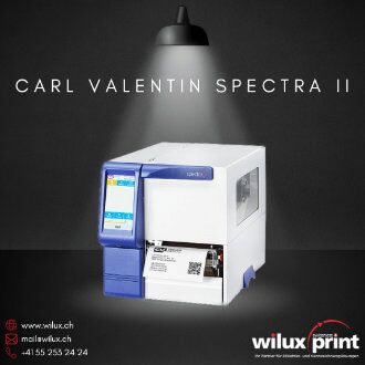 Detailansicht des Carl Valentin Spectra II Industrieetikettendruckers mit Fokus auf das intuitive Bedienfeld und die Etikettenrolle, im Lichtkegel eines Spotlichts, mit Kontaktinformationen von WILUX PRINT