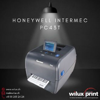 Honeywell Intermec PC43T Desktop Barcodedrucker, beleuchtet von einem Scheinwerfer auf einem Tisch, mit einem frisch gedruckten Etikett und Kontaktinformationen von WILUX PRINT