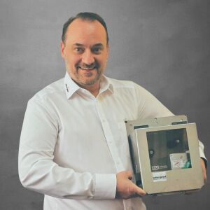 Franz Passenheim, Technischer Verkäufer bei WILUX PRINT, hält ein Hochleistungsmodul in den Händen, professionell gekleidet in einem weissen Hemd, vor einem neutralen Hintergrund.