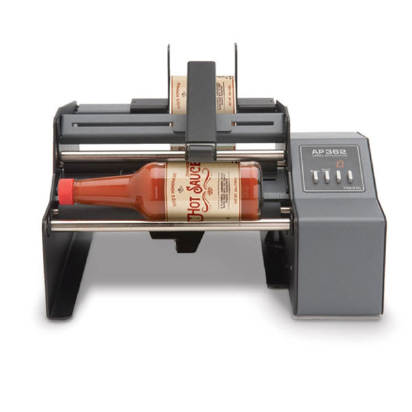 Wrap-around bottle labeler Primera AP362e in black, silver with red hot sauce bottle