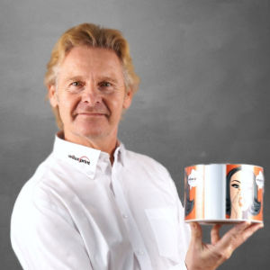 Fredy Fischbacher, Mitglied des Team WILUX PRINT und Spezialprojekte Media, hält eine bedruckte Etikettenrolle, professionell gekleidet in einem weissen Hemd, vor einem neutralen Hintergrund.